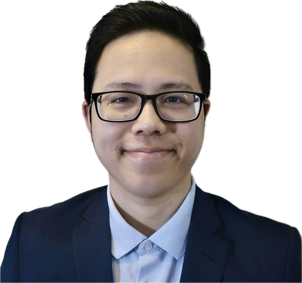 Close-up of a person with short black hair wearing black-rimmed glasses and a navy blazer, smiling softly.